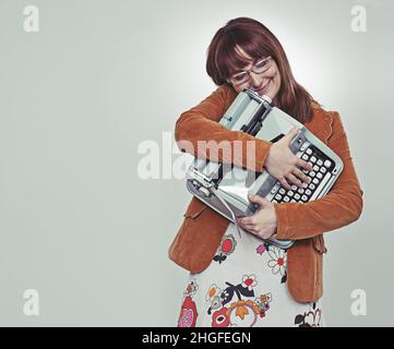 Mein Schatz Studioaufnahme einer jungen, buchhaften Frau in Retro-Kleidung, die ihre Schreibmaschine umarmte. Stockfoto