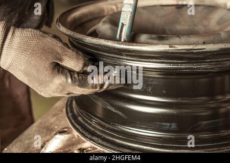 Mechaniker, der ein Ventil in ein Rad setzt, das er in Innenräumen repariert Stockfoto