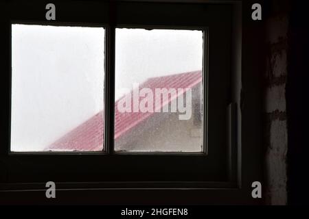 Blick auf die alte, schmutzige Fensterkonstruktion zum roten Dach Stockfoto