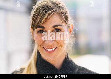 Porträt einer glücklichen Studentin, die die Kamera anschaut. Erfolgreiche stolze Frau in der City Street im Frühjahr. Zufriedene europäische Studentin in lässiger Kleidung Stockfoto