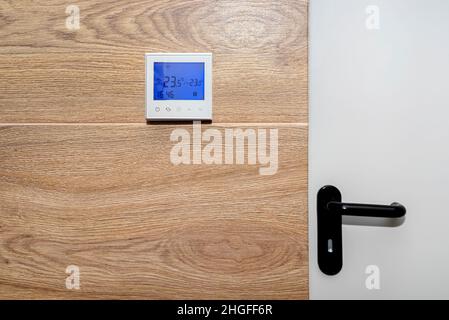 Zimmerthermostat mit einer Temperatur von 23,5 Grad Celsius an einer mit Keramikfliesen ausgekleideten Wand. Stockfoto