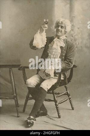 Antike Fotografie um 1910, Mann, der ein Glas in der Mode des 18.. Jahrhunderts mit Hosen, Strümpfen, Spitzen-Kravatte, Perücke, Manschetten, Und Schuhschnallen. QUELLE: ORIGINALFOTO Stockfoto