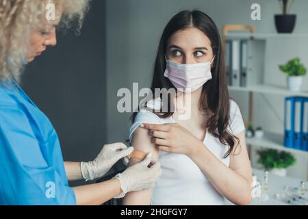 Foto mit einem Arzt, der einen Verband auf ihren Patientenarm anwendet. Arzt Impfpatient auftragen. Arztzand. Virenschutz. Covid-19 Grippeschutz Stockfoto