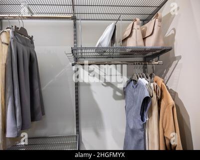 Blick auf einen großen begehbaren Schrank mit Metallregalen, in dem Kleider, Röcke, Jacken und Geldbörsen aufbewahrt werden Stockfoto