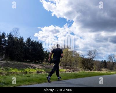 Woodinville, WA USA - ca. April 2021: Ansicht eines Mannes in schwarzer Kleidung beim Joggen auf einem Wander- und Radweg in Woodinville bei strahlender Sonne Stockfoto