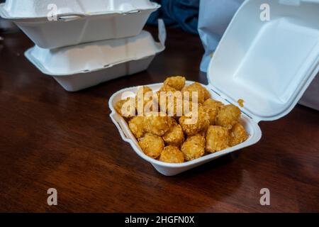 Selektiver Fokus von knusprigen, goldbraunen Tater-Tots in einem weißen Styropor-To-Go-Behälter aus einem Restaurant. Stockfoto