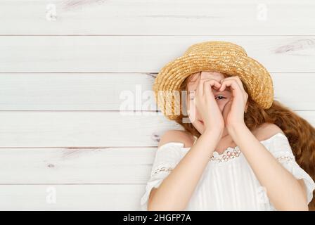 Teen girl making a heart Symbol with her hands, loying on a wooden floor. Liebe, Freunde, medizinisches Konzept. Stockfoto