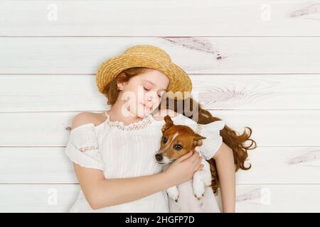 Das kleine Mädchen umarmt ihren Hund, der auf einem Holzboden liegt. Stockfoto