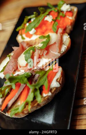 Bruschetta mit Lachs, Quark, getrockneten Tomaten und Micro Greens, auf schwarzem Hintergrund Stockfoto