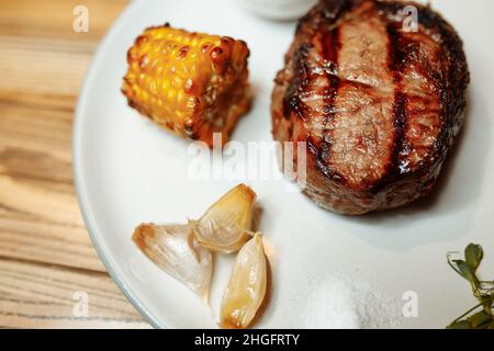 Gegrilltes Rib-Eye-Steak vom Grill, gebratenes Rib-Eye-Rindfleisch auf einem Teller mit grünem Salat. Dunkler Hintergrund Stockfoto