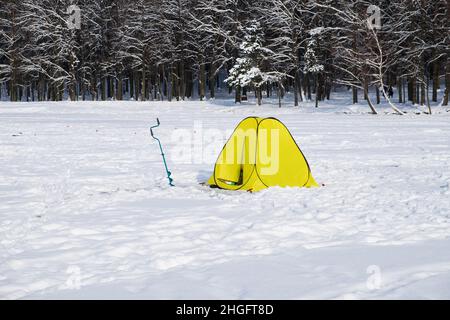 Eisfischerzelt und Eisbohrmaschine sowie ein gelbes Fischerzelt. Werkzeuge für den Winterfischer aus dem Eis. Greift An Stockfoto