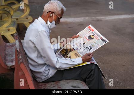 Karnataka, INDIEN - 22. Dezember 2021 : Unidentifizierter Mann sitzt bequem und liest indische Zeitung auf der Straße von Udupi. Stockfoto