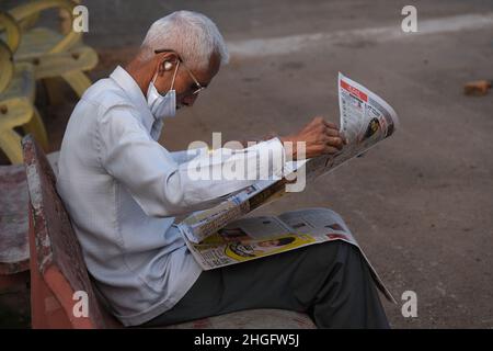 Karnataka, INDIEN - 22. Dezember 2021 : Unidentifizierter Mann sitzt bequem und liest indische Zeitung auf der Straße von Udupi. Stockfoto