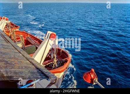 Ein orangefarbenes Rettungsboot, das an der Seite eines Kreuzschiffs über ruhigen, grauen Meeren hängt Stockfoto