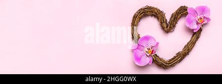 Herzförmiger Rattan-Kranz mit tropischen Orchideenblüten auf rosa Hintergrund Draufsicht Flat Lay Holiday Card Happy Valentine's day, love con Stockfoto