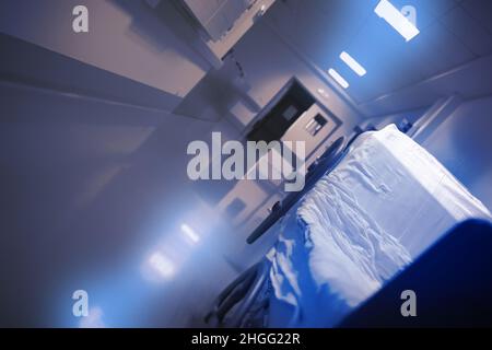 Leere Liege mit einem zerknitterte Laken in der langen Krankenhaushalle. Stockfoto