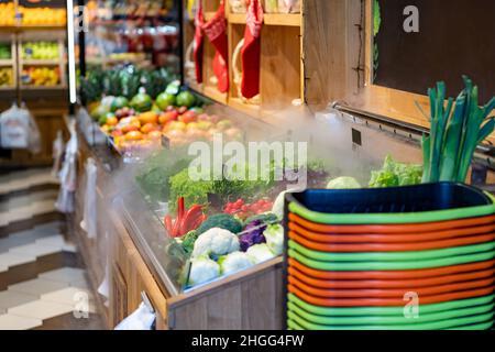 Lokaler Frischmarkt mit Obst und Gemüse in den Regalen. Einkaufskörbe. Befeuchter für Grünpflanzen. Stockfoto