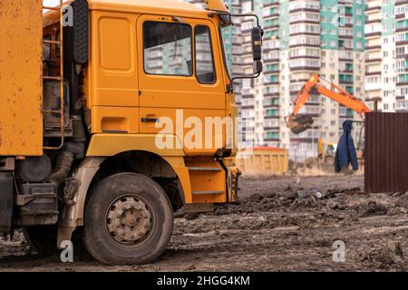 Bagger gräbt den Boden für die Gründung und den Bau eines neuen Gebäudes. Bagger beladen den Sand auf die Muldenkipper auf der Baustelle. Masse Stockfoto