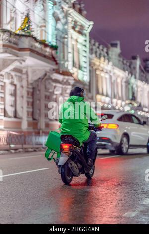 Food Delivery Boy auf dem Roller in der Nacht mit isothermen Lebensmittel-Fall. Stockfoto