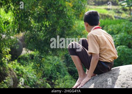 Einsame Kinder setzen sich auf den großen Stein Stockfoto
