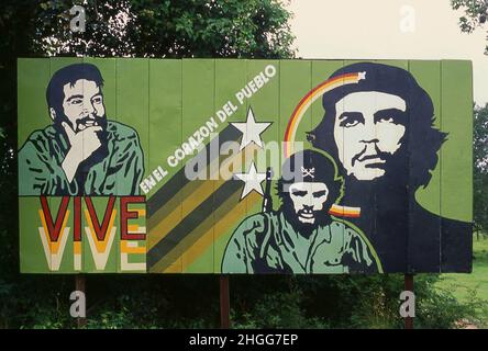 Kuba: "Er lebt in den Herzen des Volkes", ein Che Guevara-Plakat vor einer kleinen Stadt in der Provinz Matanzas. Während ihres Aufenthalts in Mexiko-Stadt traf Che Guevara (1928 - 1967) Raúl und Fidel Castro, schloss sich ihrer Bewegung vom 26th. Juli an und segelte an Bord der Yacht Granma nach Kuba, mit der Absicht, den von den USA unterstützten kubanischen Diktator Fulgencio Batista zu stürzen. Guevara wurde unter den Aufständischen prominent, wurde zum zweiten Befehlshaber befördert und spielte eine entscheidende Rolle in der siegreichen zweijährigen Guerillakampagne, die das Batista-Regime absetzte. Stockfoto