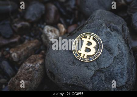 Bitcoin Krypto-Münze mit Platz für Text. Nahaufnahme einer einzelnen Gold-BTC-Kryptowährung auf Felsen im Freien. Foto mit niedriger Tonart für Banner und Nachrichten. Stockfoto