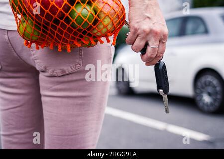 Frau, die den Autoschlüssel in der Hand hielt, nachdem sie im Supermarkt einkaufen war. Defokussed Auto auf dem Parkplatz Stockfoto