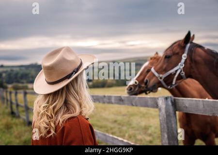 Frau mit Cowboyhut, die ihre Pferde auf der Weide ansieht. Cowgirl in der Tierfarm Stockfoto