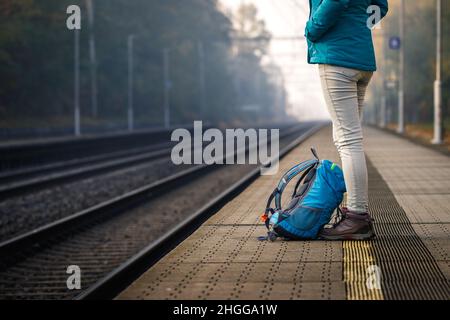 Alleinreisende, die am leeren Bahnhof auf den Zug warten. Frau mit Rucksack, die auf dem Bahnsteig steht Stockfoto