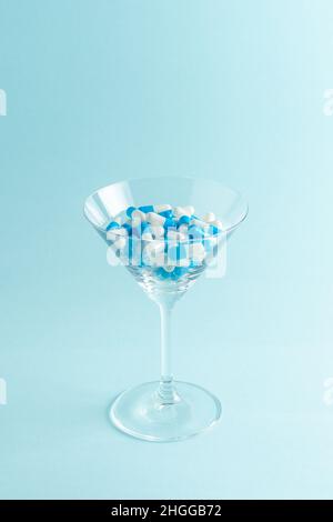 Martiniglas voller farbenfroher Pillen auf blauem Hintergrund. Kreative Komposition. Stockfoto
