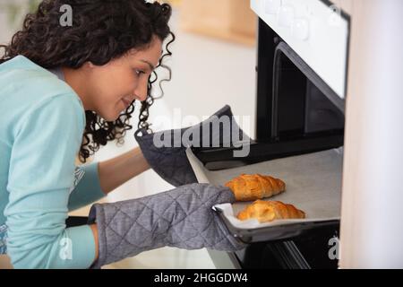 Frau, die drinnen Teller mit Croissants in die Mikrowelle legte Stockfoto