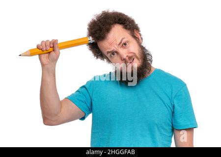 Bärtiger nachdenklicher Mann mit witzigem lockigem Haar mit großem Bleistift, isoliert auf weißem Hintergrund. Stockfoto