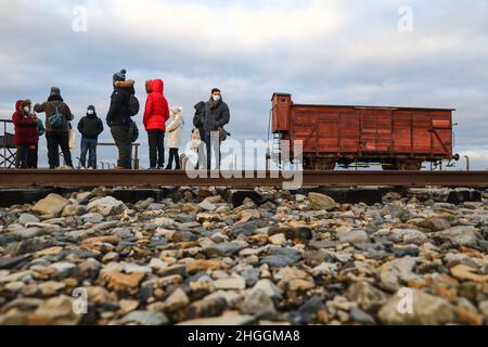 Die Besucher stehen neben einem originalen Eisenbahnwagen, der am 2. Januar 2022 für Deportationen im ehemaligen KZ-Vernichtungslager Auschwitz II-Birkenau in Oswiecim, Polen, verwendet wurde. Stockfoto