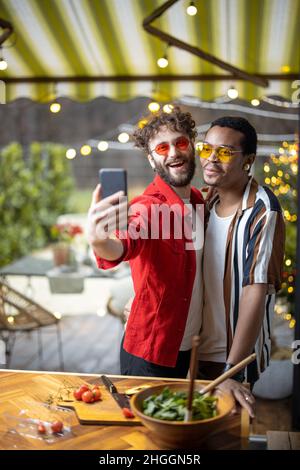 Zwei bunt gekleidete, stylische Jungs, die in Innenräumen Selfie am Telefon machen Stockfoto