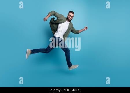 Profil Foto von fröhlich nett Kerl springen sportlich Lauf tragen specs grün Hemd Jeans isoliert blau Farbe Hintergrund Stockfoto