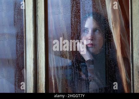 Gelangweilte Frau schaut während des Regens aus dem Fenster auf die Straße Stockfoto