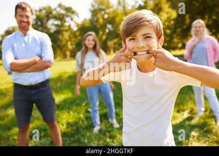 Junge macht Gesichter auf einer Wiese mit Eltern und Schwester im Hintergrund Stockfoto
