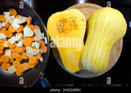 butternusskürbis (Cucurbita moschata), geschälter Butternusskürbis, in der Mitte geteilt, neben einer Pfanne mit Karotten und Pastinaken Stockfoto
