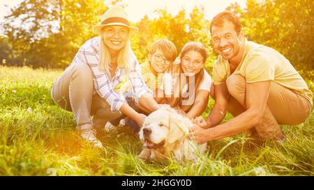 Glückliche Familie mit zwei Kindern streicheln Hund als Haustier im Garten Stockfoto