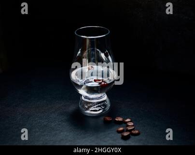 Chiaroscuro-Bild von Sambuca in einem einfachen Glas mit Kaffeebohnen . Dunkler Hintergrund mit viel Platz und einer Handvoll Kaffeebohnen im Vordergrund. Stockfoto