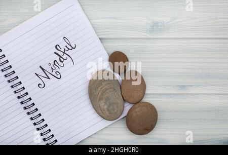Notizbuch mit dem Wort achtsam darauf geschrieben. Auf einer Pastell-Holzmaserung mit Strandfeeling Stockfoto