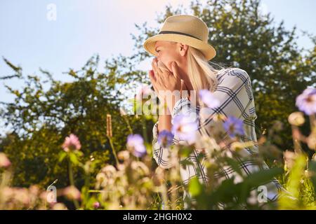 Junge Frau mit laufender Nase oder Heuschnupfen beim Niesen in ein Taschentuch auf einer Wiese Stockfoto