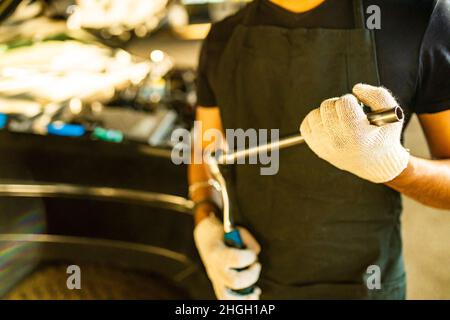 lateinischer hispanischer Automechaniker in Uniform untersucht ein Auto, während er im Autodienst arbeitet Stockfoto