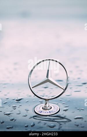 Nahansicht Des Metallsternlogos Von Mercedes Benz Auf Der Feuchten Haube Des Blauen Autos Nach Dem Regen. Stockfoto