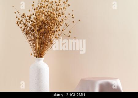 Satin Tuch Produktdisplay Podium mit Vase von getrockneten Flachs Blumen auf beigem Hintergrund. Konzept der Produktpräsentation. Minimalistischer Style. Stockfoto