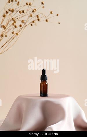 Massage ätherisches Öl in Bernstein Glas Tropfflasche auf Satin-Stoff runden Podium auf beigem Hintergrund mit getrockneten Flachs Blumen. NATURKURORT Beauty Produ Stockfoto