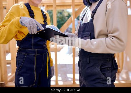 Zwei Junge Spezialisten Prüfen Die Baustellendokumentation Für Holzhäuser. Immobilienprojekt mit Bauingenieur. Mann und Frau im Schnitt Stockfoto