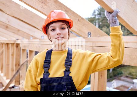 Seriöse Konstrukteurs-Ingenieurin weiblich in New Wohnbau Haus Rahmen. Holzbaustelle. Attraktive kaukasische Dame in orangefarbenem Helm Stockfoto
