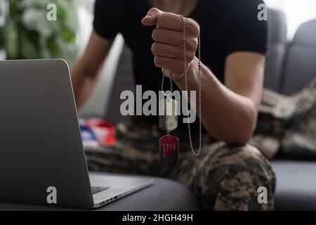 Patriotischer Militärangehöriger im Headset, der in der Nähe der amerikanischen Flagge auf einen Laptop schaut Stockfoto