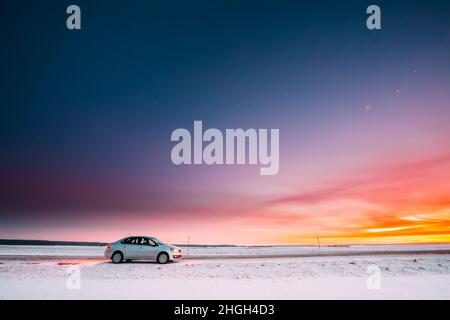 Volkswagen Polo Auto Limousine Parken auf Einer Straße der Country Road auf Einem Hintergrund des dramatischen Sonnenuntergang Himmel in der Wintersaison Stockfoto